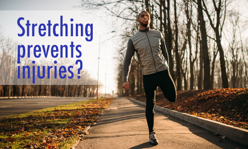 In this image a man is outdoors stretching his leg in preparation for a run.